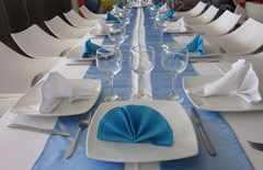 Biały stół z białą zastawą i serwetami w kolorze błękitnym.