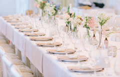 Stół na przyjęciu pierwszokomunijnym z dekoracjami w kolorze różowym i bukiecikami kwiatowymi w wazonach.