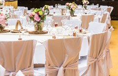 Sala z okrągłymi stołami na 10 osób przybranymi na biało i krzesłami pokrytymi różowym materiałem.