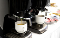 Ekspresy kawowe nalewające kawę do białych filiżanek.