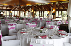 Sala weselna z okrągłymi stołami z zastawa w kolorze białym i różowymi elementami dekoracyjnymi.
