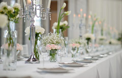 Zblizenie przybranego na biało stołu z zastawa i wazonikami z biało-rózowymi kwiatami.